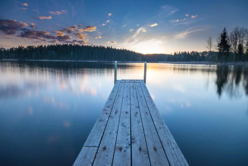 Puinen laituri järven rannalla, aurinko on laskemassa.